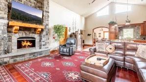 A stone fireplace, leather sofa, and a television mounted on the wall. - Canyon Crest Lodge. Hot Tub, Game Room, and Views. (Big Bear Lake)