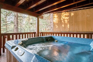 A hot tub with a wooden deck and a view of trees.
