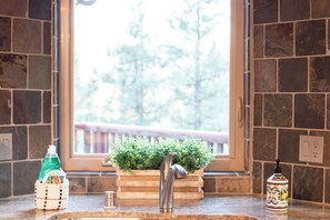 A kitchen with a stone backsplash, a window with a view of greenery, a wooden countertop, and a stainless steel faucet.