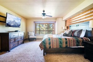 A bedroom with a bed, a dresser, a television, a ceiling fan, a window, and a chair.