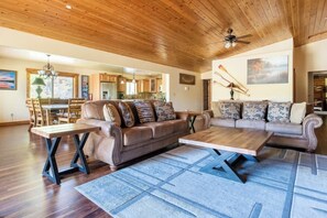 A spacious living area with a wooden ceiling, a sofa set, a coffee table, and a dining table.