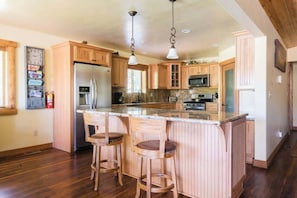 A kitchen with wooden cabinets, a stainless steel refrigerator, a microwave, and a large island with bar stools.