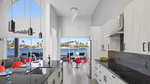 Una cocina moderna con una isla grande, un comedor con sillas rojas y vistas al mar.