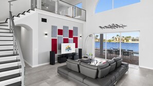 Un salón amplio con un sofá gris, un televisor de pantalla plana y un balcón con vista al agua.