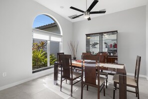 Un coin repas avec une table à plateau en verre, des chaises en bois et un ventilateur de plafond.