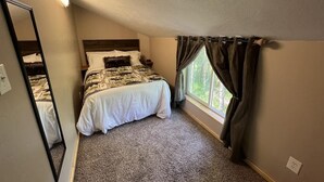 Un dormitorio con cama, mesita de noche, espejo, ventana con cortinas y una lámpara en el techo.