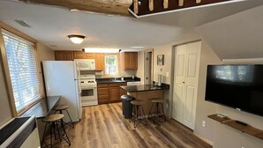 Una cocina compacta con piso de madera, refrigerador, estufa y taburetes de bar.