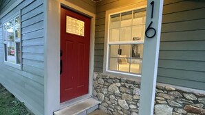 Una casa con puerta roja, pared de piedra y el número 16 en la fachada.