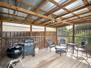 A covered patio with a grill, chairs, and a table.