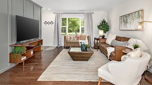 Una sala de estar moderna con un televisor de pantalla plana, mueble de madera para entretenimiento y un ventanal con cortinas.