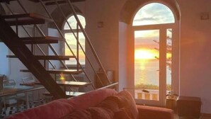 A room with a red sofa, a staircase, and a large arched window with a sunset view.
