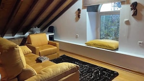 A cozy attic bedroom with a sofa, a small table, and a window with a view of trees.