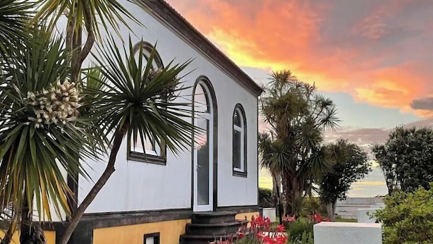 A white building with arched windows, surrounded by tropical plants and red flowers.