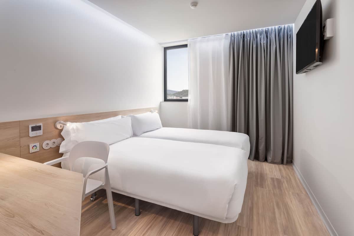 Una habitación de hotel moderna con una cama, un escritorio y un televisor montado en la pared.