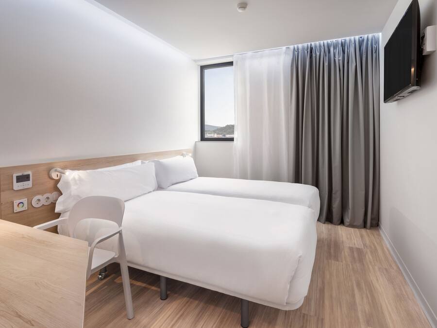 Una habitación de hotel moderna con una cama, un escritorio y un televisor montado en la pared.