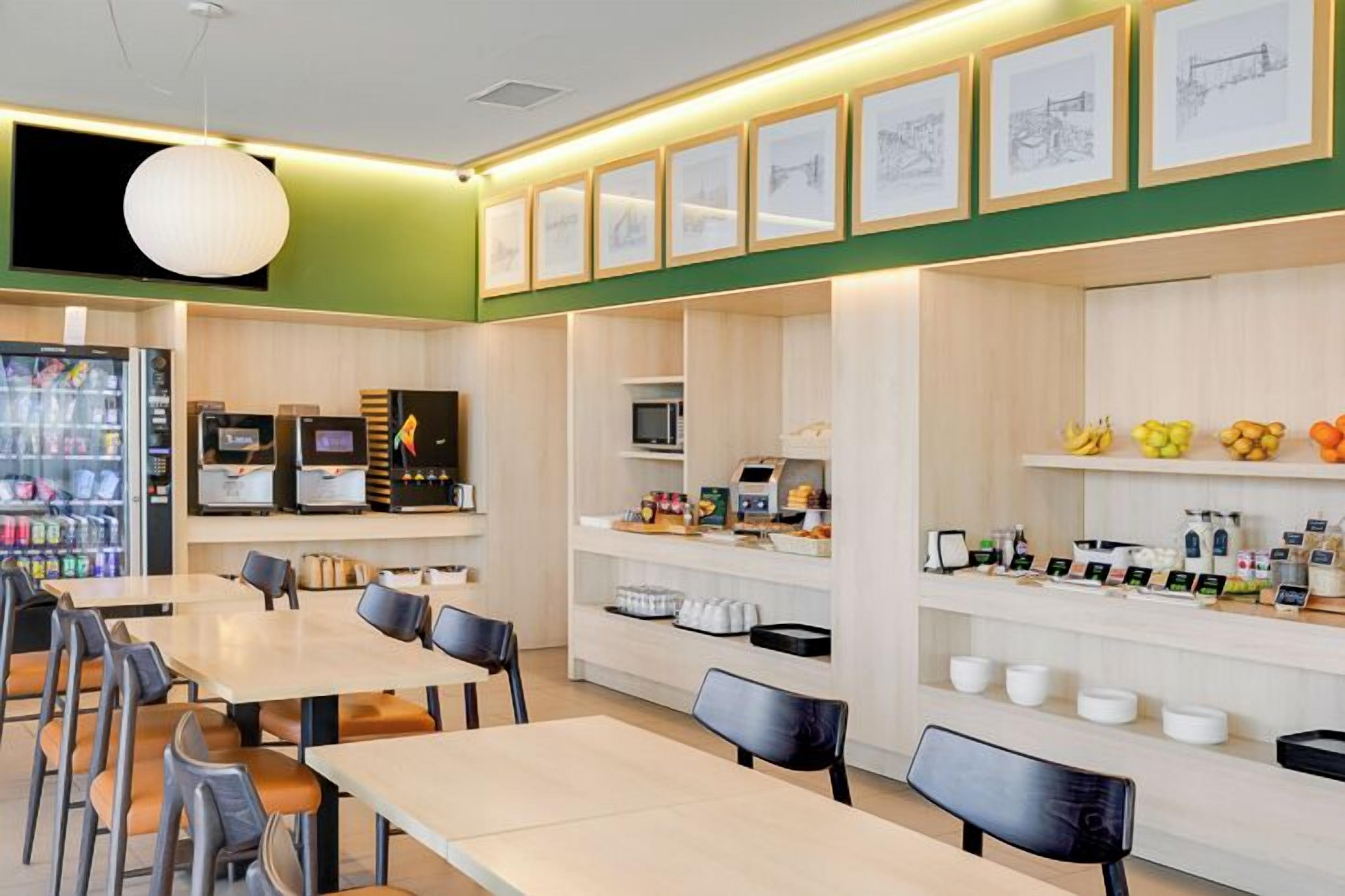 A modern cafe with tables and chairs, a coffee machine, a microwave, and a fruit display.