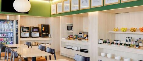 A modern cafe with tables and chairs, a coffee machine, a microwave, and a fruit display.