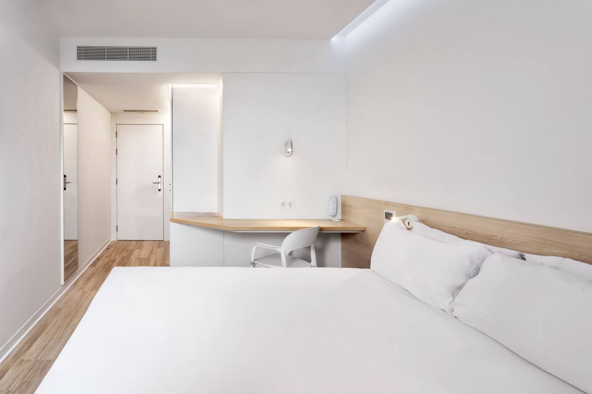 Una habitación de hotel moderna con una cama grande, un escritorio de madera y una silla blanca.