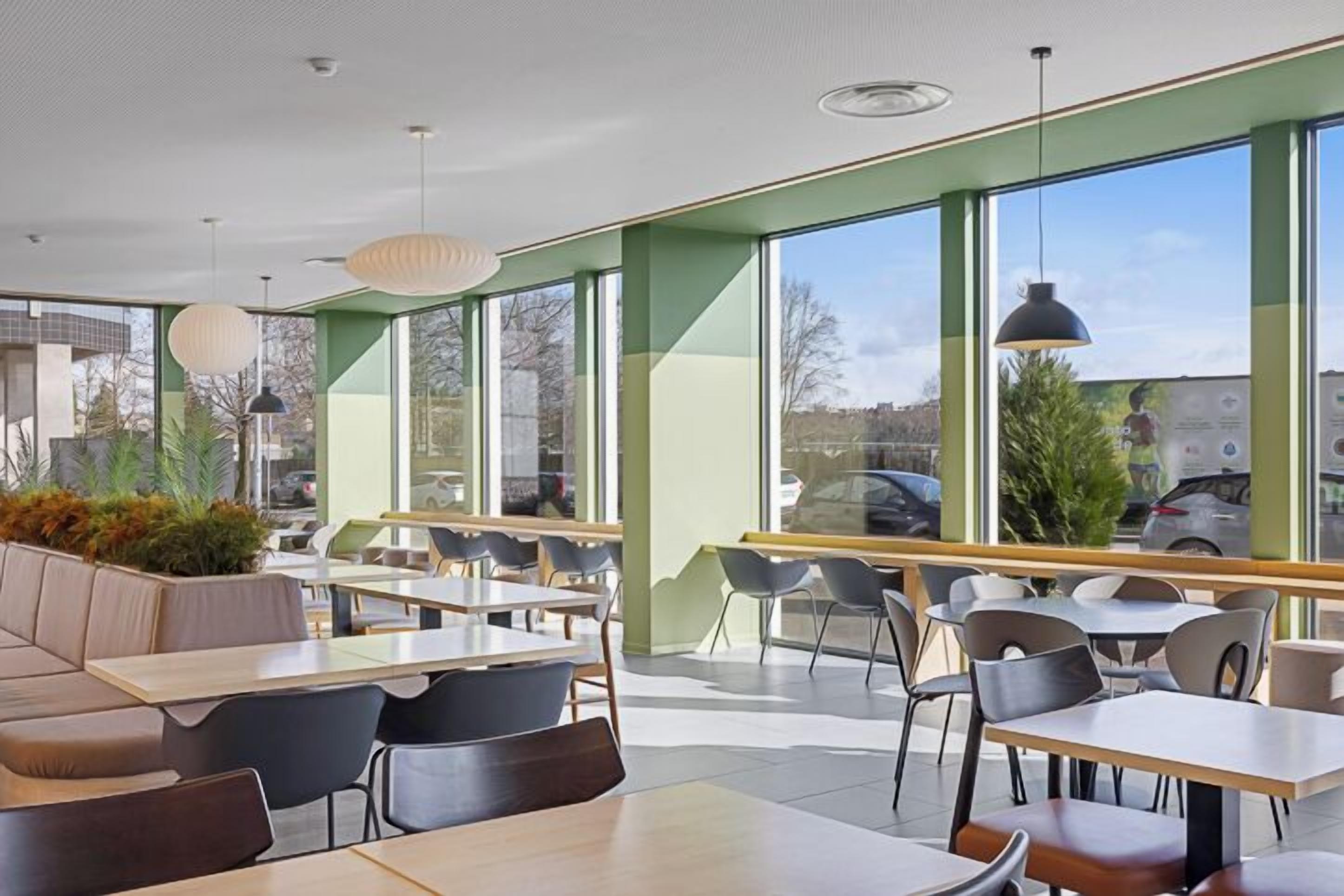 A modern cafe with large windows, seating areas, and pendant lighting.