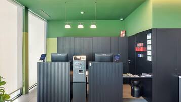A reception area with a green wall, three pendant lights, and a reception desk with a computer and a cash register.