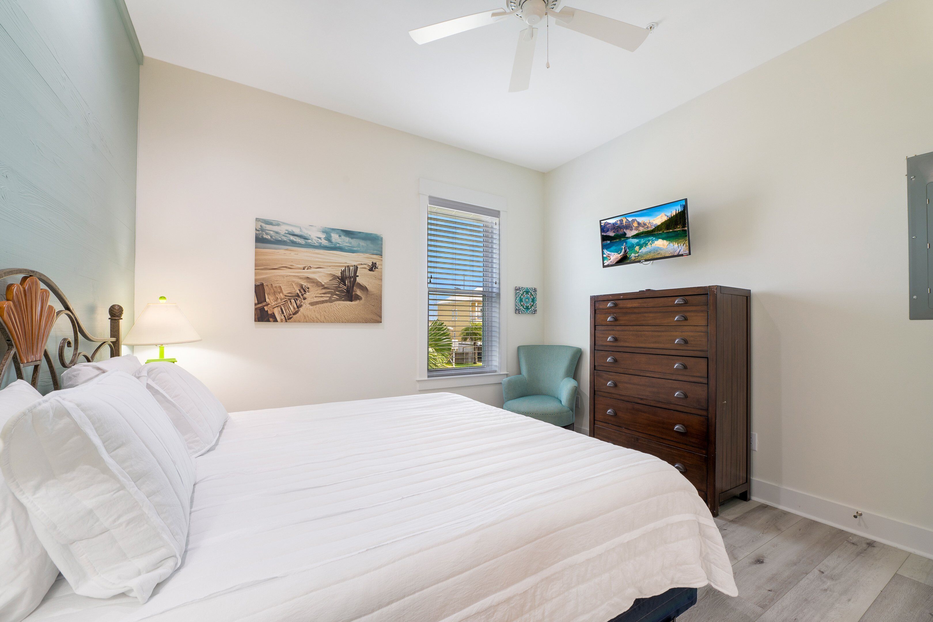 A bedroom with a bed, a dresser, a chair, a window with blinds, and wall art.