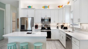 Una cocina moderna con armarios blancos, electrodomésticos de acero inoxidable y una isla central con taburetes.