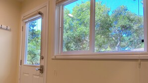 Um quarto com porta, janela com vista para árvores, sofá azul e tapete estampado.