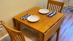 Uma mesa de jantar de madeira com duas cadeiras, um tapete pequeno e uma janela com persianas.