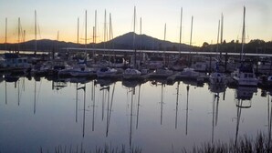 Uma marina com vários barcos atracados, água calma refletindo os barcos e uma montanha ao fundo.