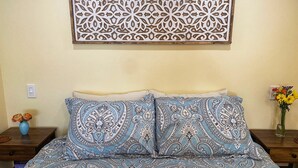 Quarto com cama, painel decorativo na parede, um vaso com flores e uma mesa de cabeceira.