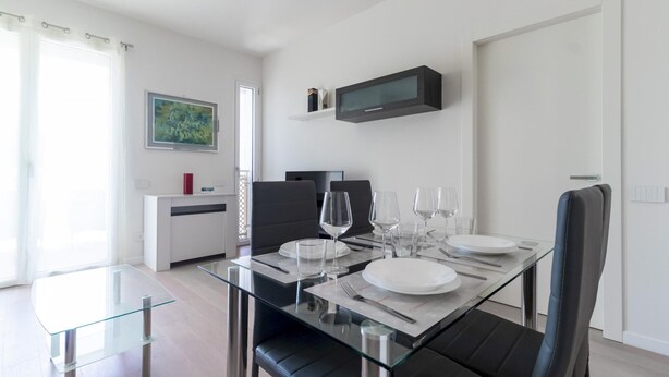 Un comedor moderno con una mesa de vidrio, sillas negras y un televisor de pantalla plana en la parte superior.