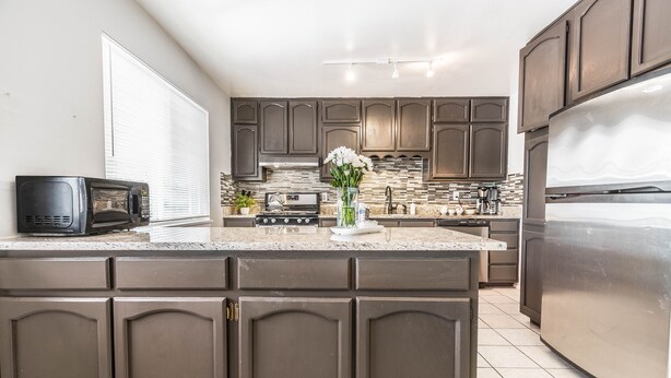 A modern kitchen with dark cabinetry, a stainless steel refrigerator, and a granite countertop. -  POOL, Sleeps 10, CENTRALY LOCATED, game room, pets. great for LONG TERM stays. (El Paso)