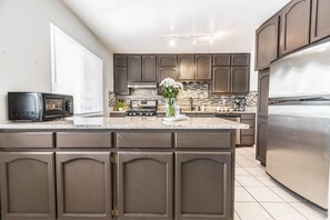 A modern kitchen with dark cabinetry, a stainless steel refrigerator, and a granite countertop. - POOL, Sleeps 10, CENTRALY LOCATED, game room, pets. great for LONG TERM stays. (El Paso)