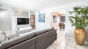 A modern living room with a grey sofa, a flat-screen TV, a large vase, and a dining area in the background. -  POOL, Sleeps 10, CENTRALY LOCATED, game room, pets. great for LONG TERM stays. (El Paso)