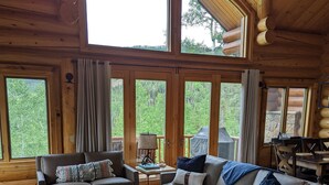 L’intérieur d’un chalet confortable, avec une grande fenêtre, un canapé, une table basse et un fauteuil en cuir.