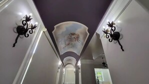 Ein Flur mit hoher Decke, dekorativen Wandleuchten und einem Wandgemälde.
