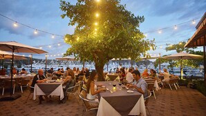An outdoor dining area with tables and chairs under string lights, overlooking a marina with boats. - Colina 9E 2 bdr 2 Bath Family (Jacó)