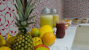 A kitchen counter with various fruits, including a pineapple, lemons, and oranges, and two glass containers with a yellow liquid. - Pousada Estrela Azul (João Pessoa)