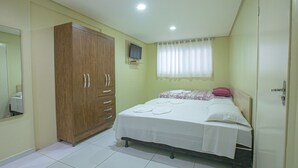 A bedroom with a bed, a wardrobe, a television, and a window with curtains. - Pousada Estrela Azul (João Pessoa)