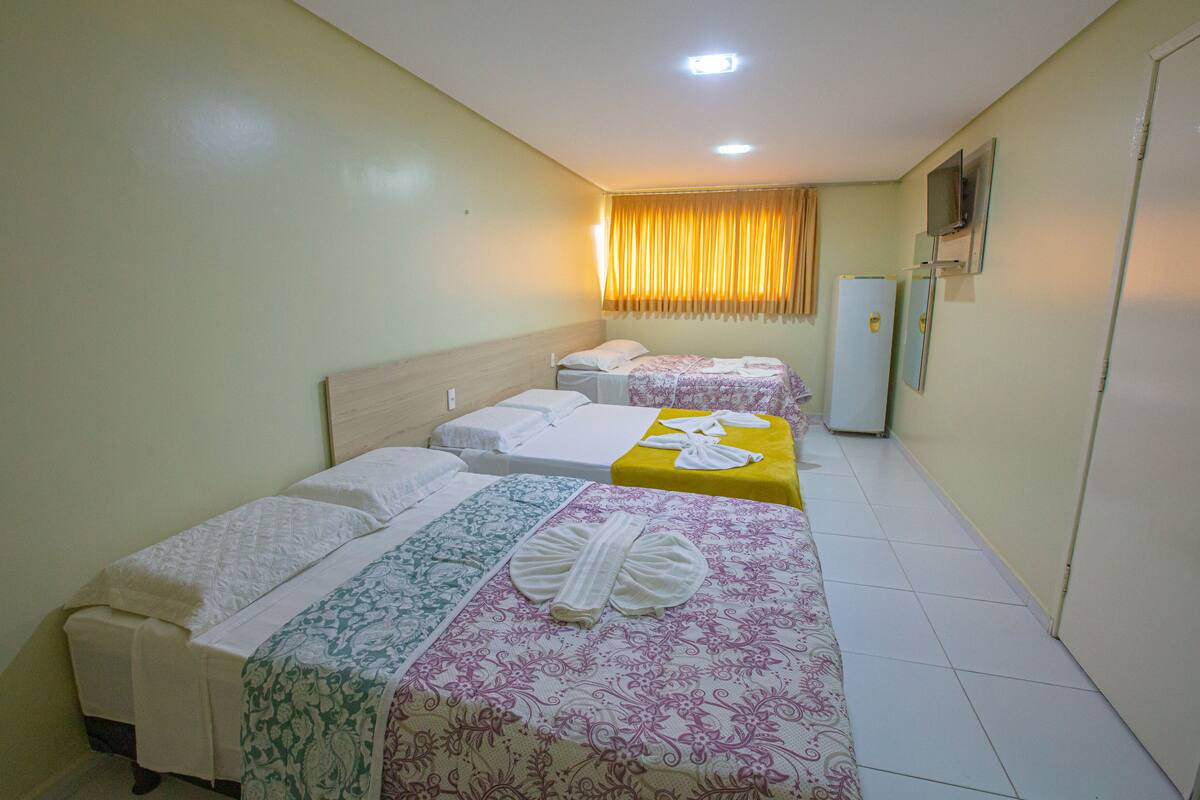 A hotel room with two beds, a refrigerator, and a television on the wall.