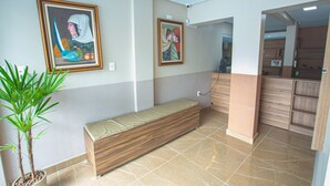 A reception area with a bench, two framed artworks, a potted plant, and a wooden counter. - Pousada Estrela Azul (João Pessoa)