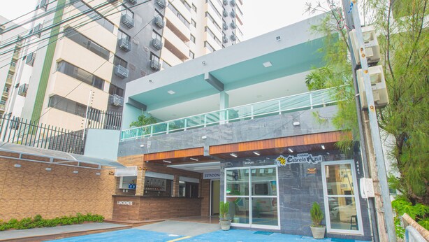 A modern building with a covered entrance, a parking area, and a sign indicating a business or service area. - Pousada Estrela Azul (João Pessoa)