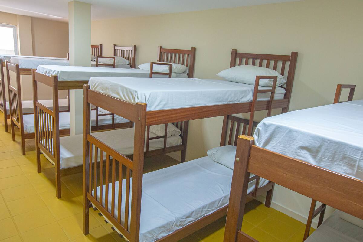 A dormitory room with bunk beds and wooden chairs.