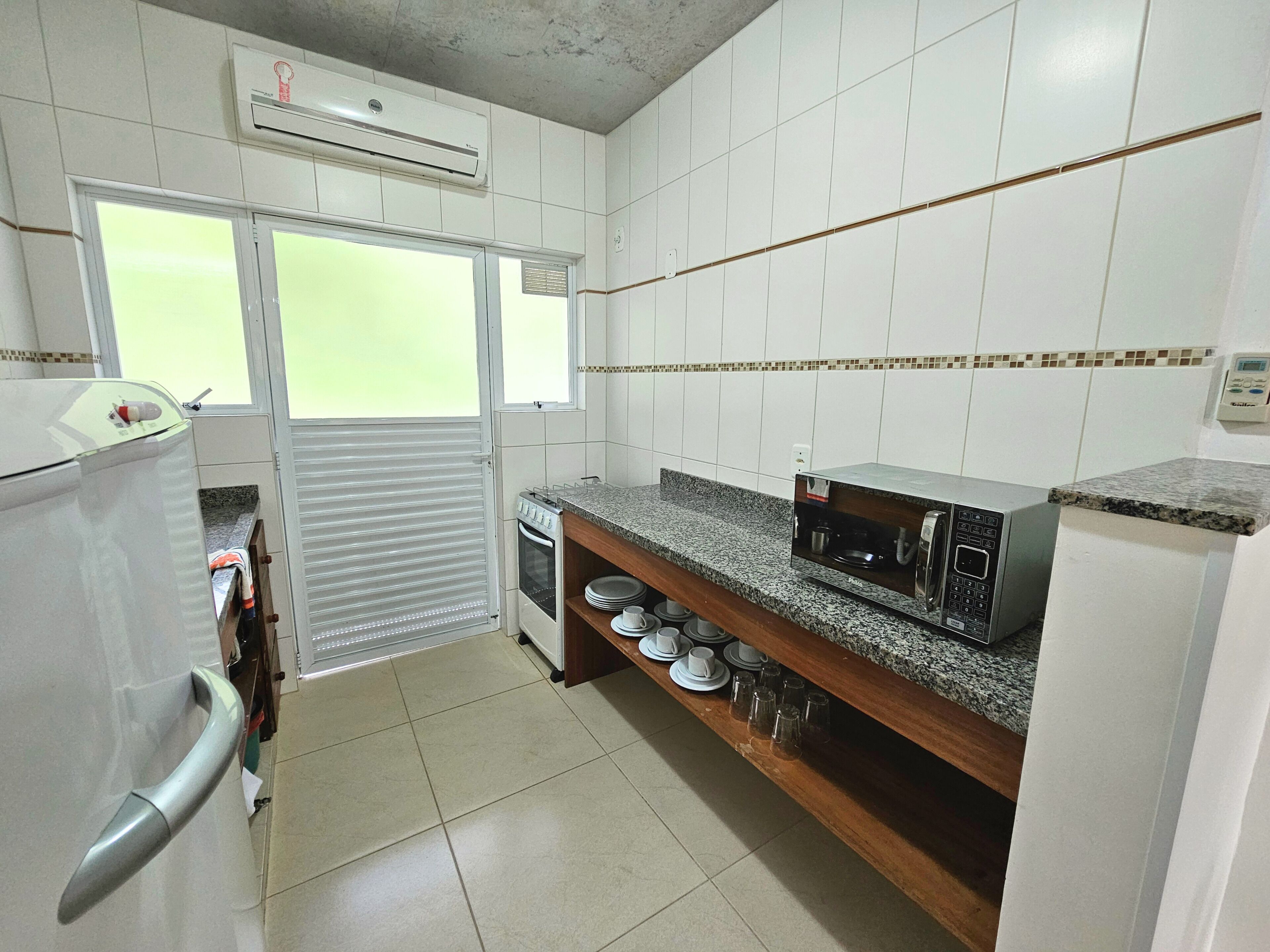 A kitchen with white tiled walls, a built-in oven, a microwave, and a stainless steel refrigerator.