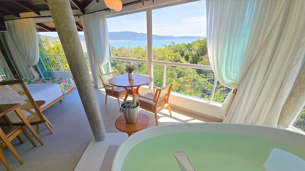 Una habitación con una bañera grande, una mesa de comedor con sillas y vistas al mar y a las colinas.