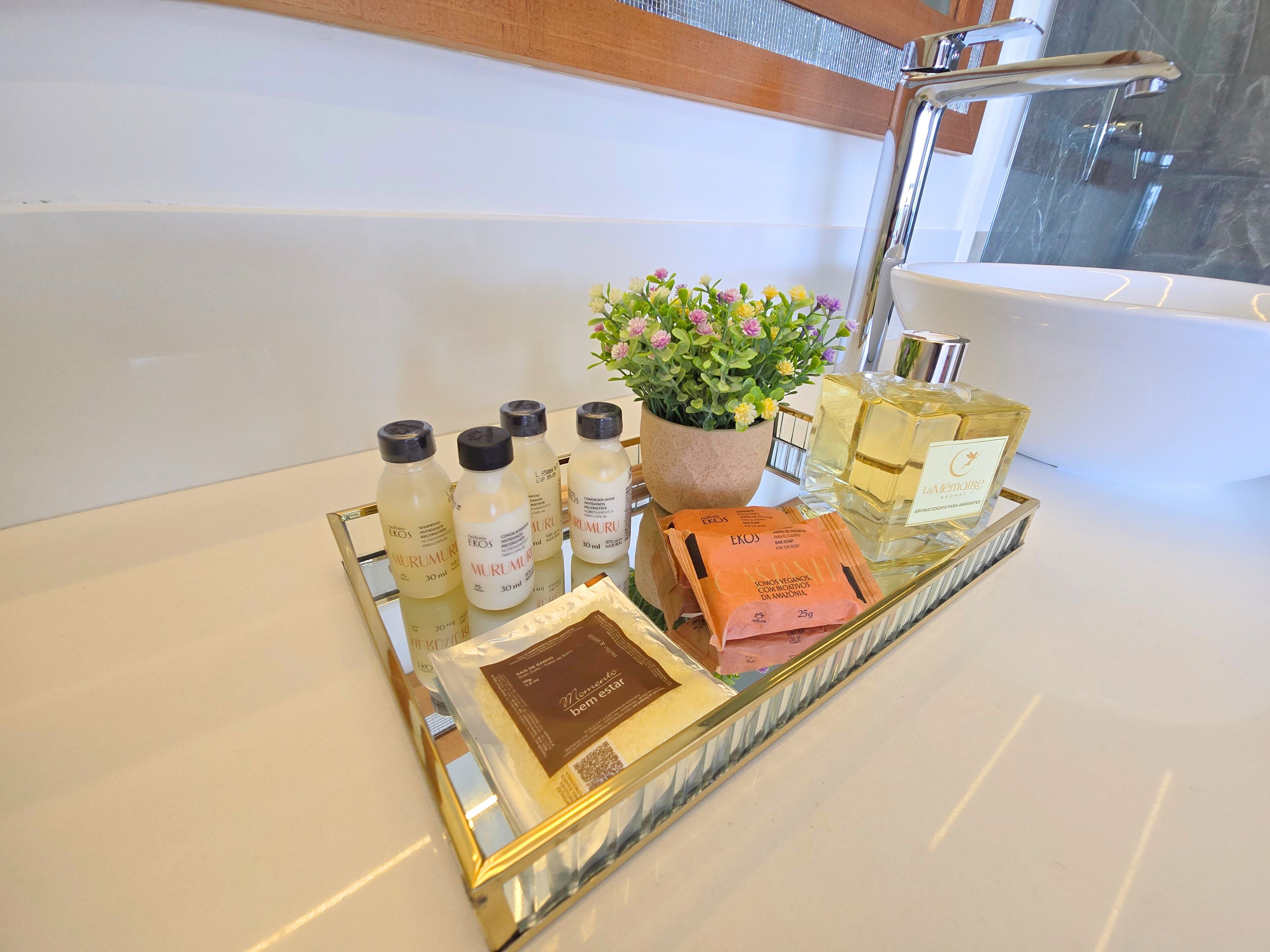 A bathroom vanity with a tray holding toiletries, a potted plant, and a bottle of perfume.