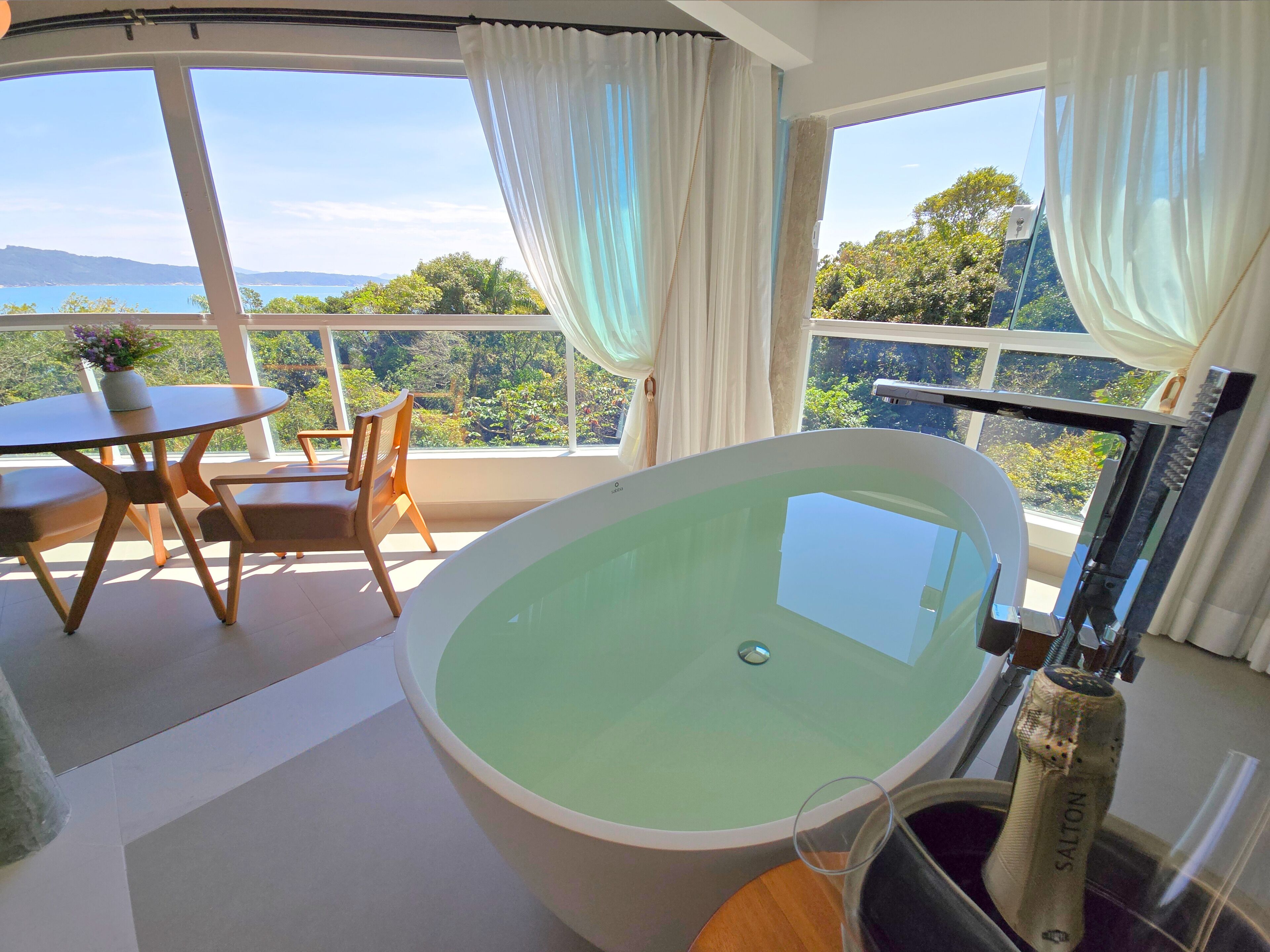 A modern bathroom with a freestanding bathtub, a glass shower enclosure, and a view of the sea.