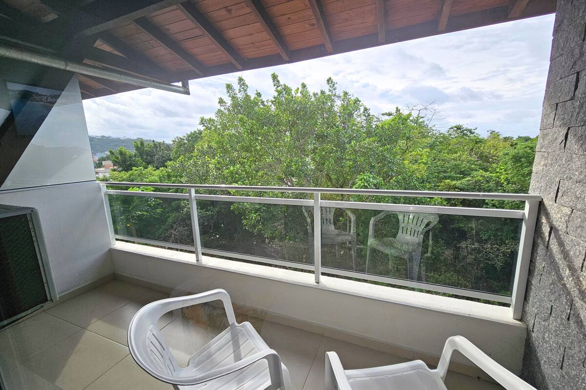 Varanda com vista para árvores e céu aberto. Há duas cadeiras de plástico branco e um corrimão de metal.