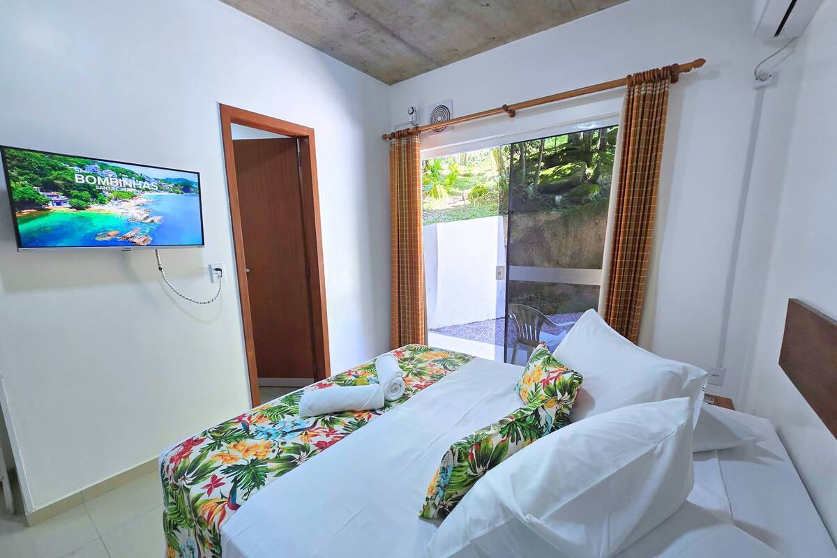 Quarto de hotel com cama, televisão na parede e porta de vidro corria para o exterior.