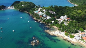 Vista aérea de una zona costera con playa, barcos y edificios rodeados de vegetación.